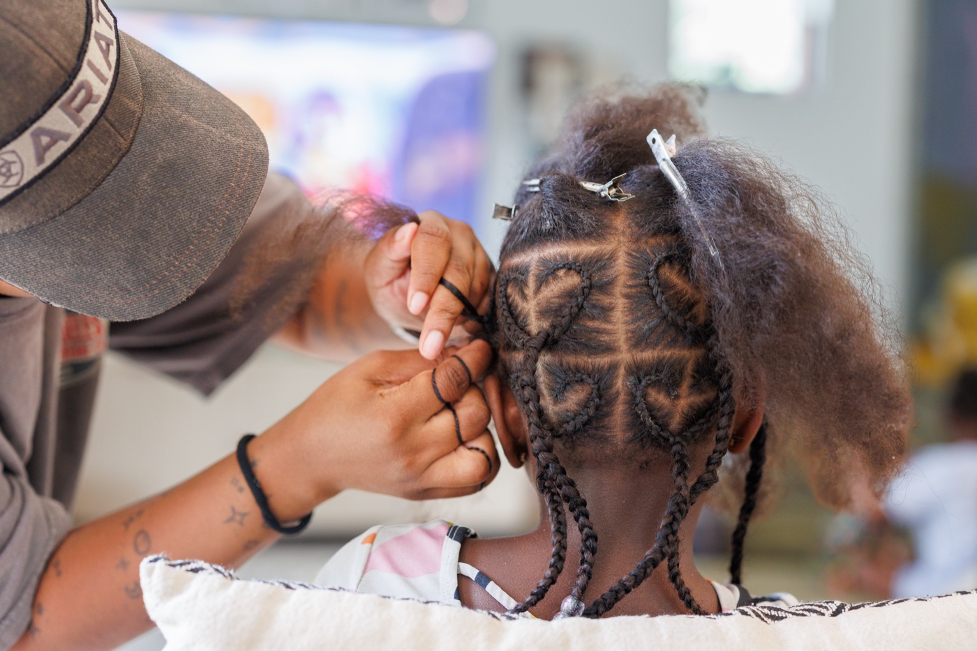 A caregiver braiding a child's hair into heart-shaped cornrows.